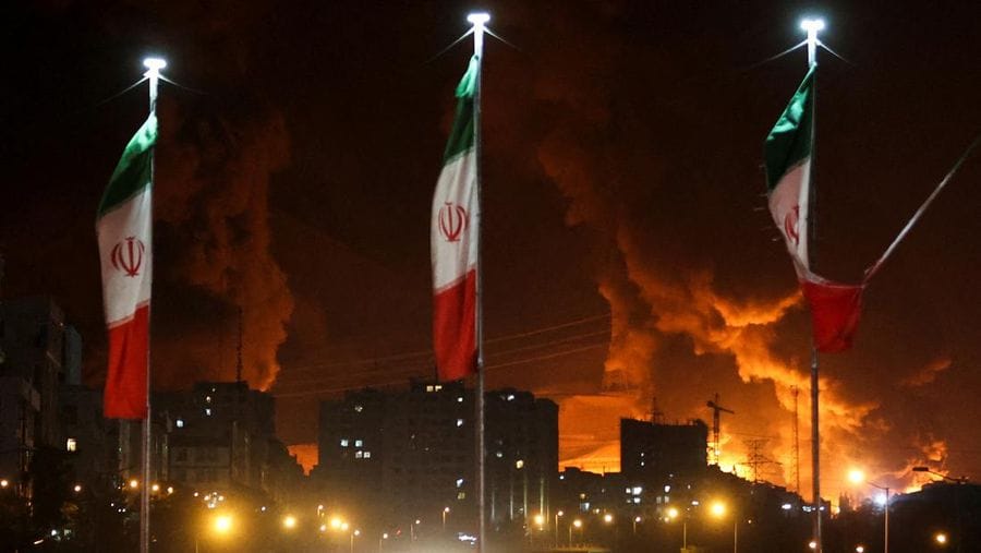 Foto: Bendera Iran berkibar saat api dan asap dari serangan Israel terhadap depot minyak Sharan membubung, menyusul serangan Israel terhadap Iran, di Teheran, Iran, 15 Juni 2025. (via REUTERS/Majid Asgaripour)